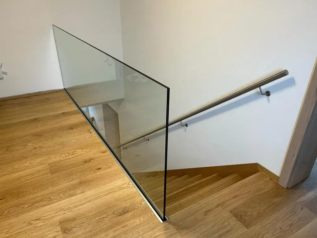 Eine Holztreppe mit Glasgeländer und Edelstahlhandlauf.