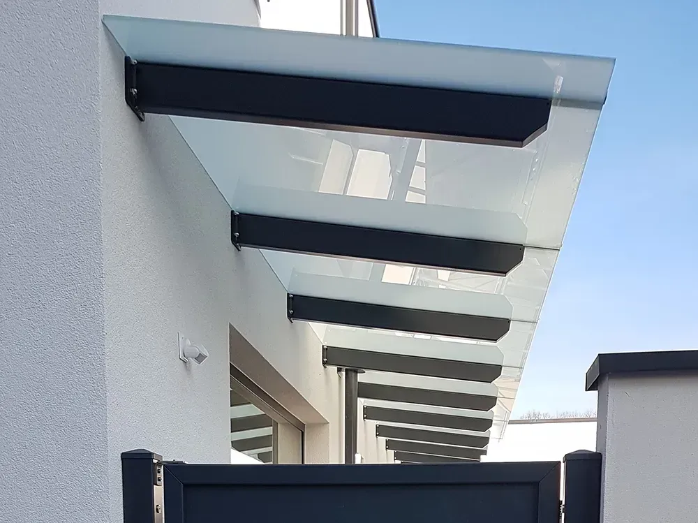 An der Seite eines Gebäudes neben einem Tor ist ein Glasdach angebracht.