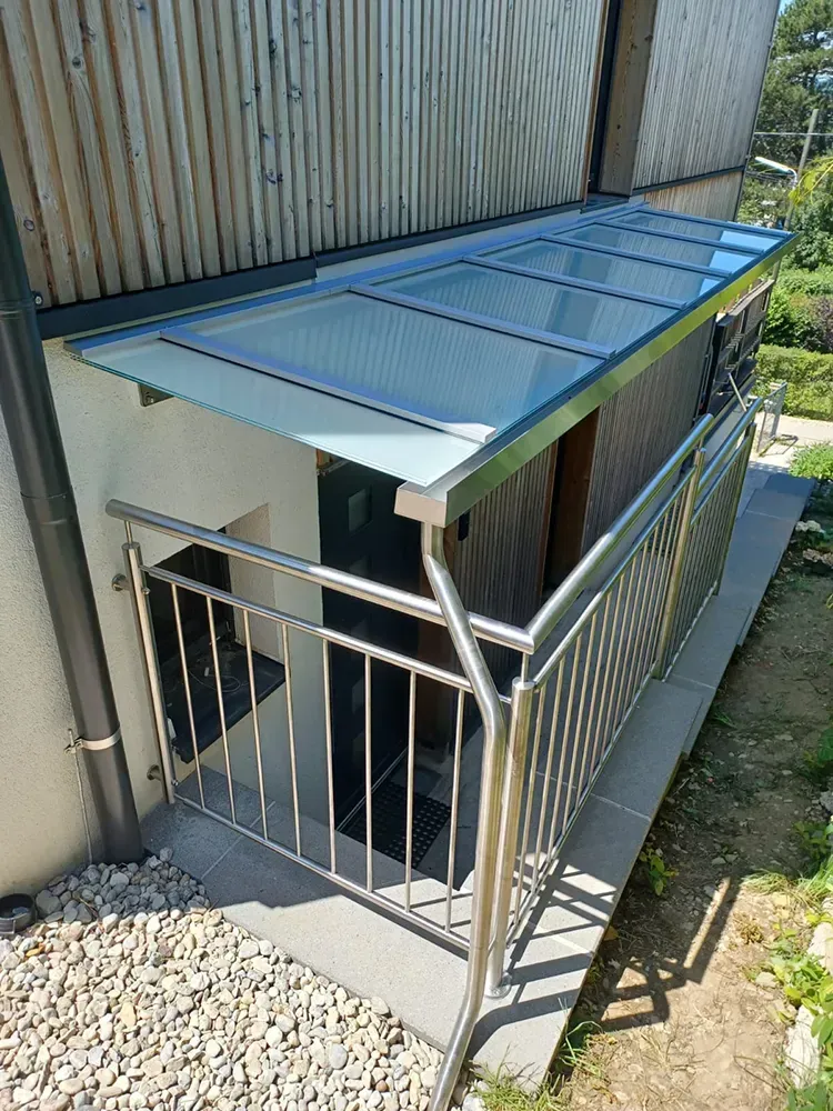 Ein Edelstahlgeländer mit einem Glasdach darüber.