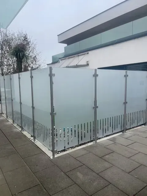 Ein Glaszaun umgibt ein Gebäude auf einem Gehweg.