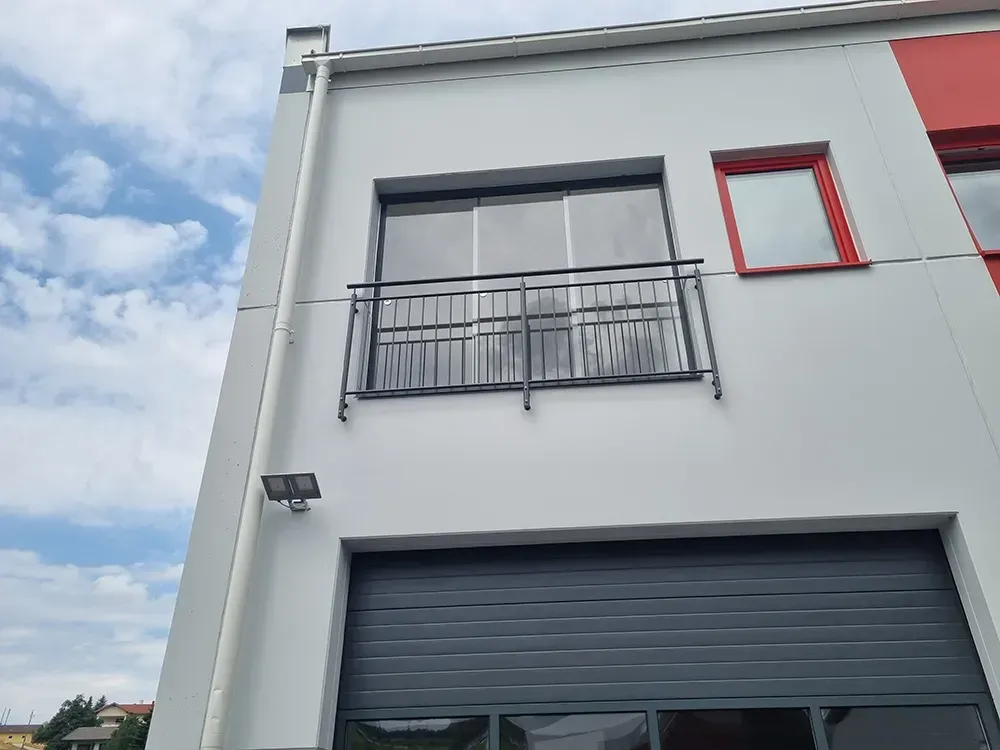 Ein weißes Gebäude mit einem schwarzen Garagentor und einem Balkon.