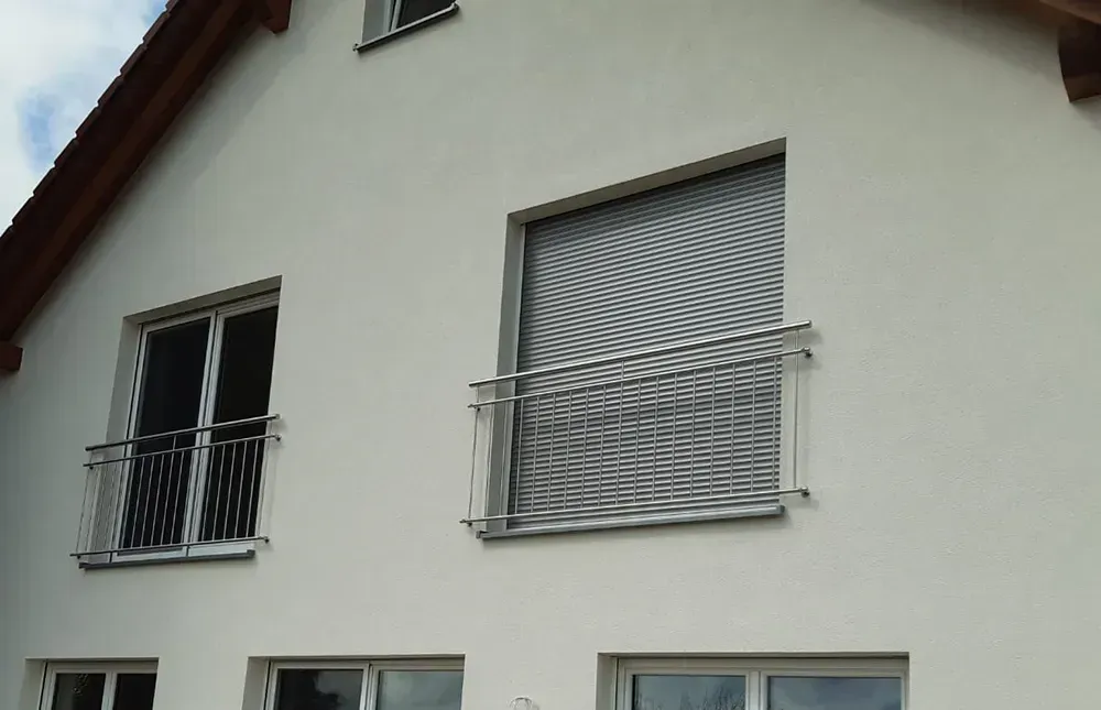 Ein weißes Haus mit zwei Fenstern und einem Metallgeländer