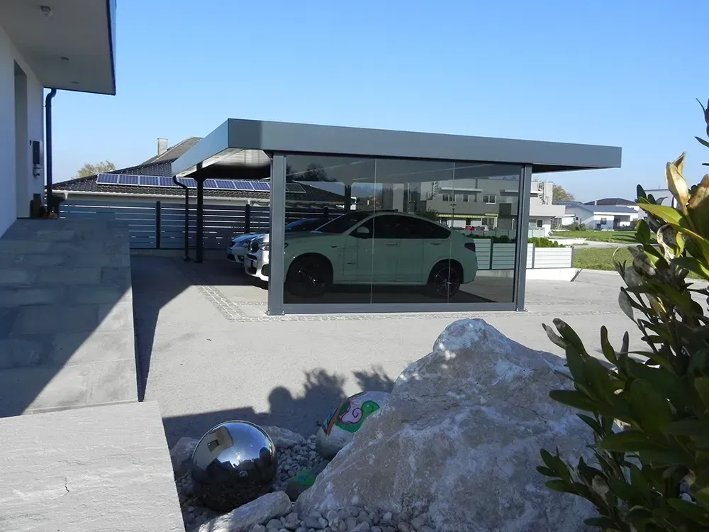 Ein Auto ist unter einem Glascarport vor einem Haus geparkt.