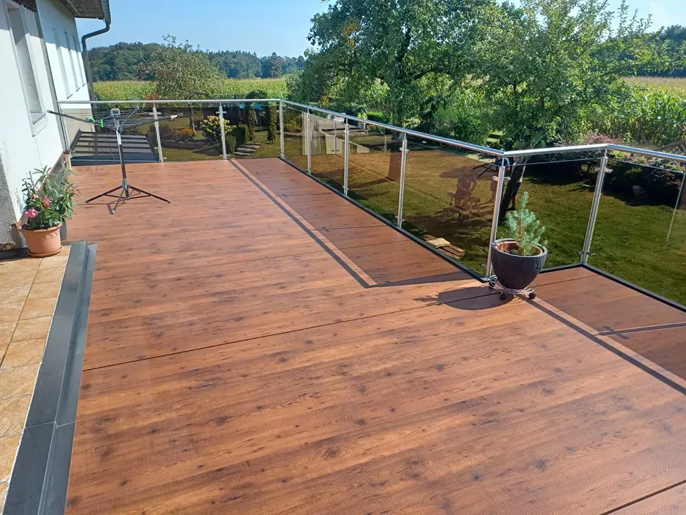 Ein Holzdeck mit Glasgeländer und einer Topfpflanze darauf.