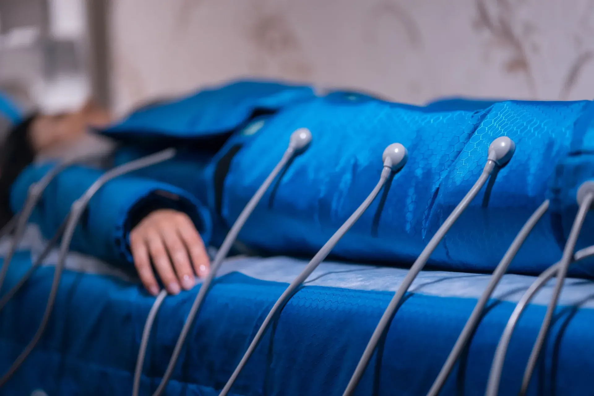 Una persona tumbada con un traje de compresión azul para terapia, con varios tubos conectados a sus compartimentos.