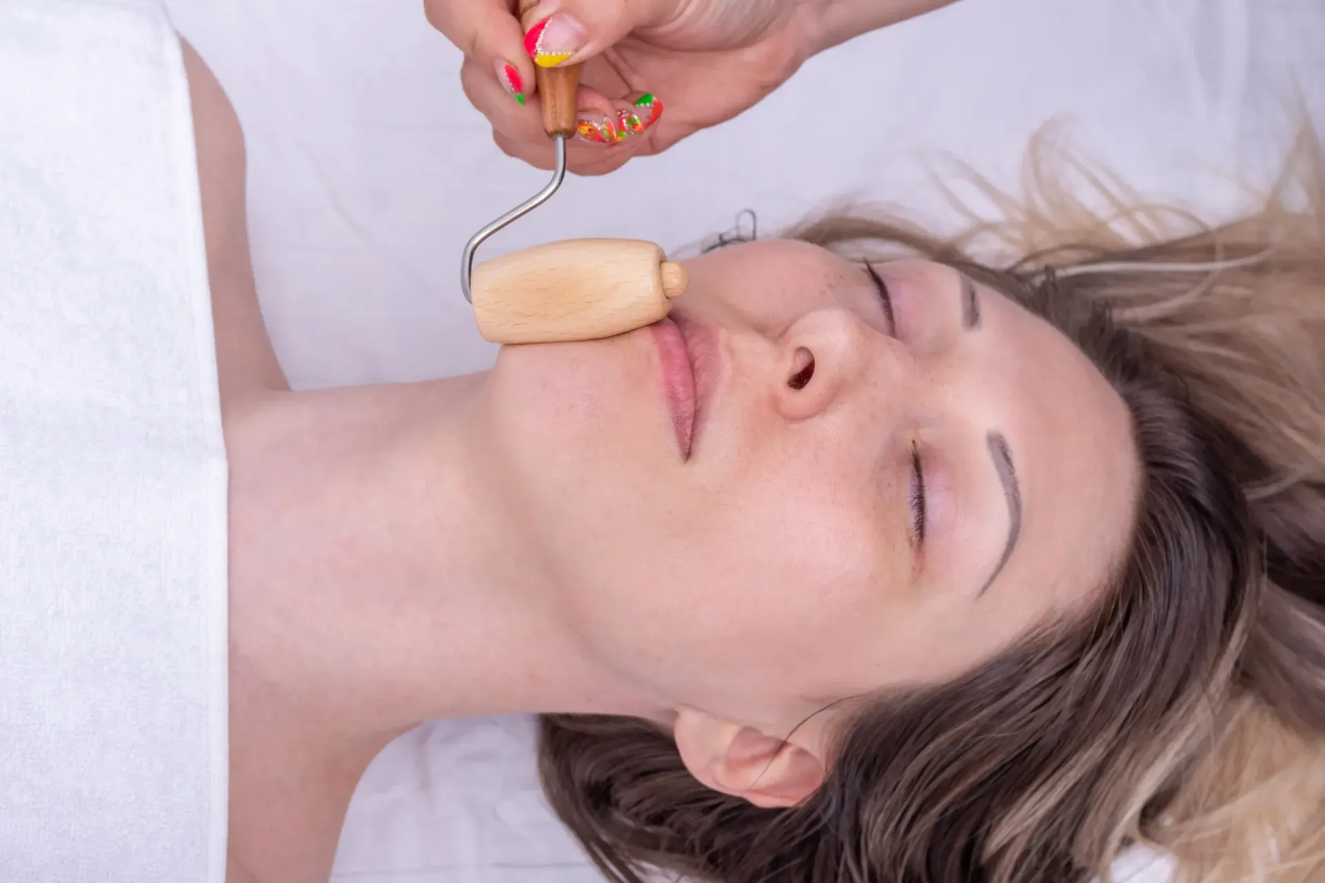 Una persona recibe un masaje facial con un rodillo de madera.