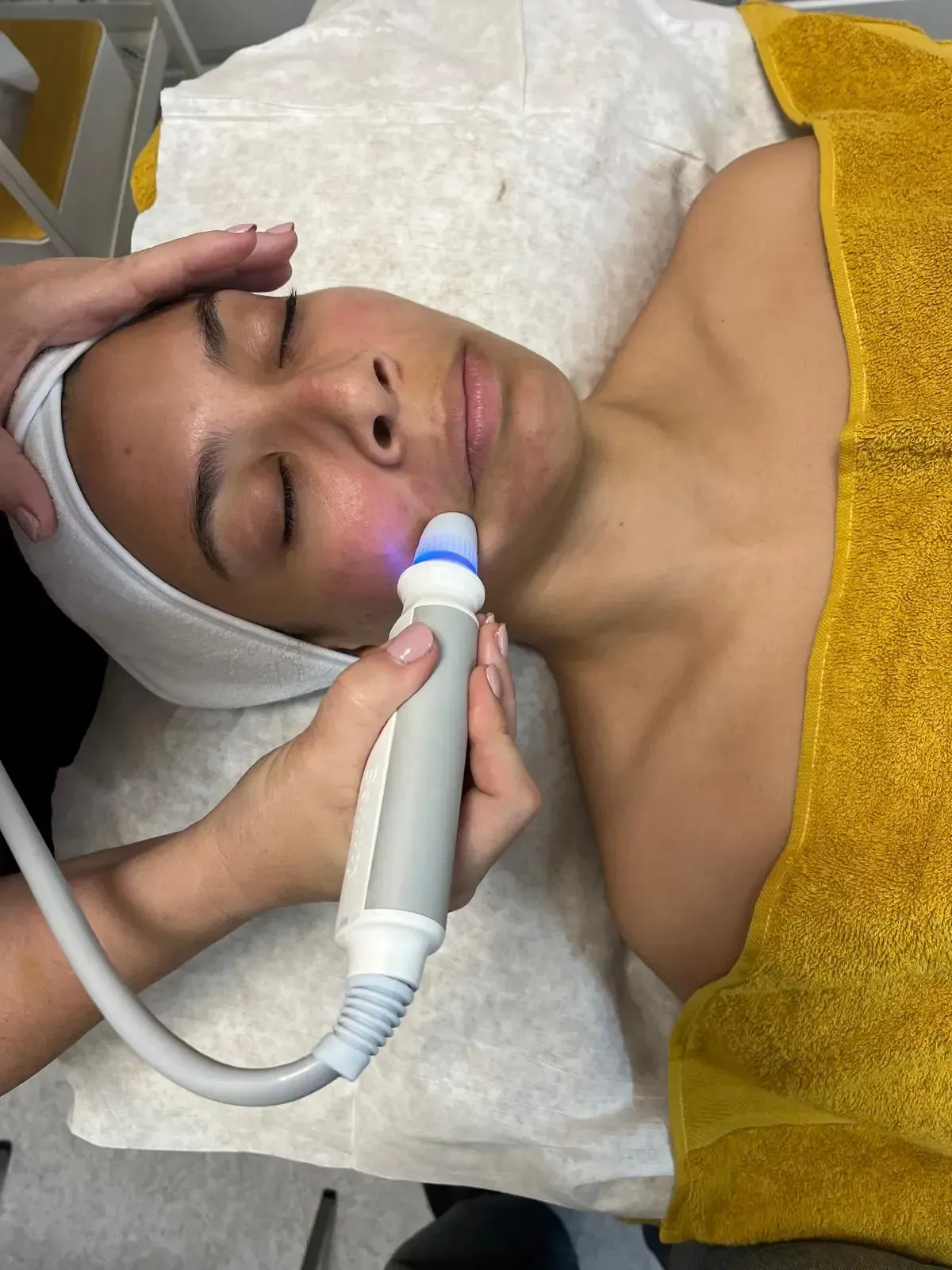 Una esteticista profesional utiliza un dispositivo portátil de luz azul en la mejilla 