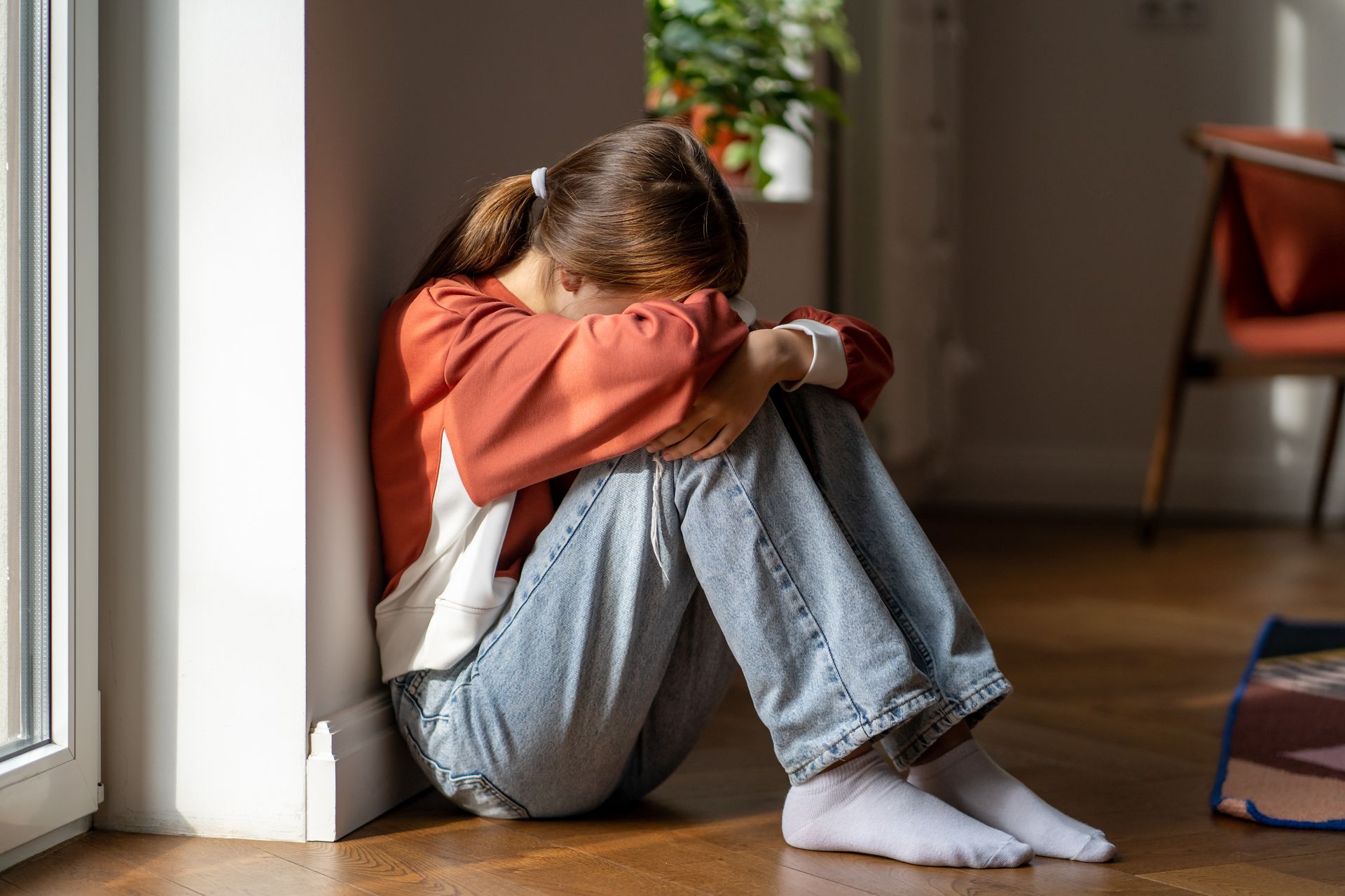Una niña está sentada en el suelo en la esquina de una habitación.