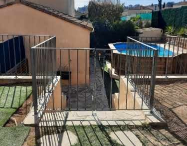 Une clôture en métal entoure un jardin avec une petite piscine et une maison.