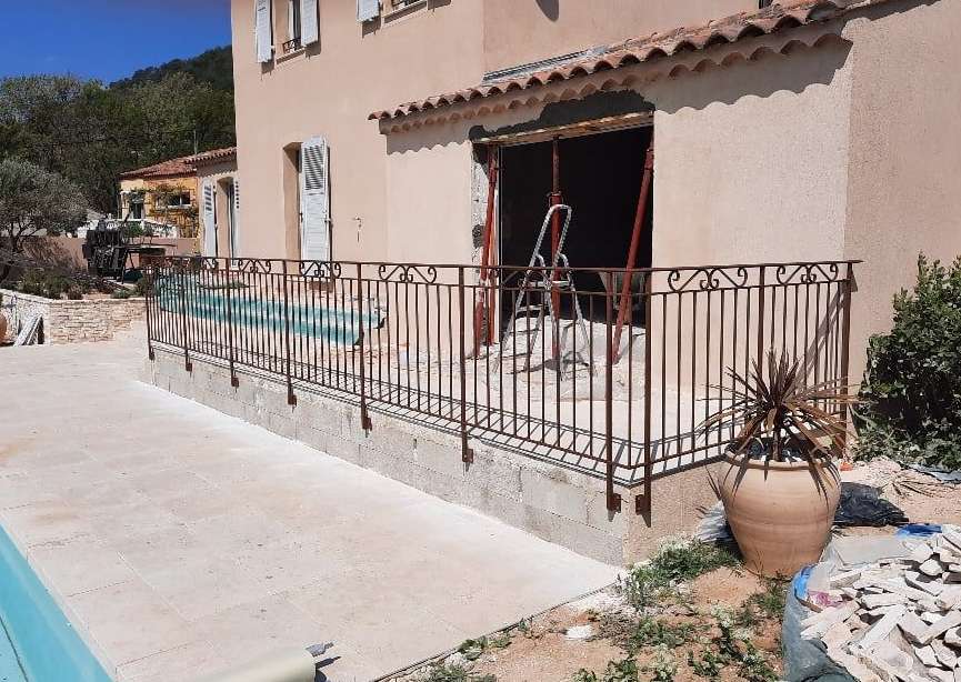Vue extérieure d'une maison avec piscine, terrasse et balustrade en fer forgé. Matériaux de construction visibles.