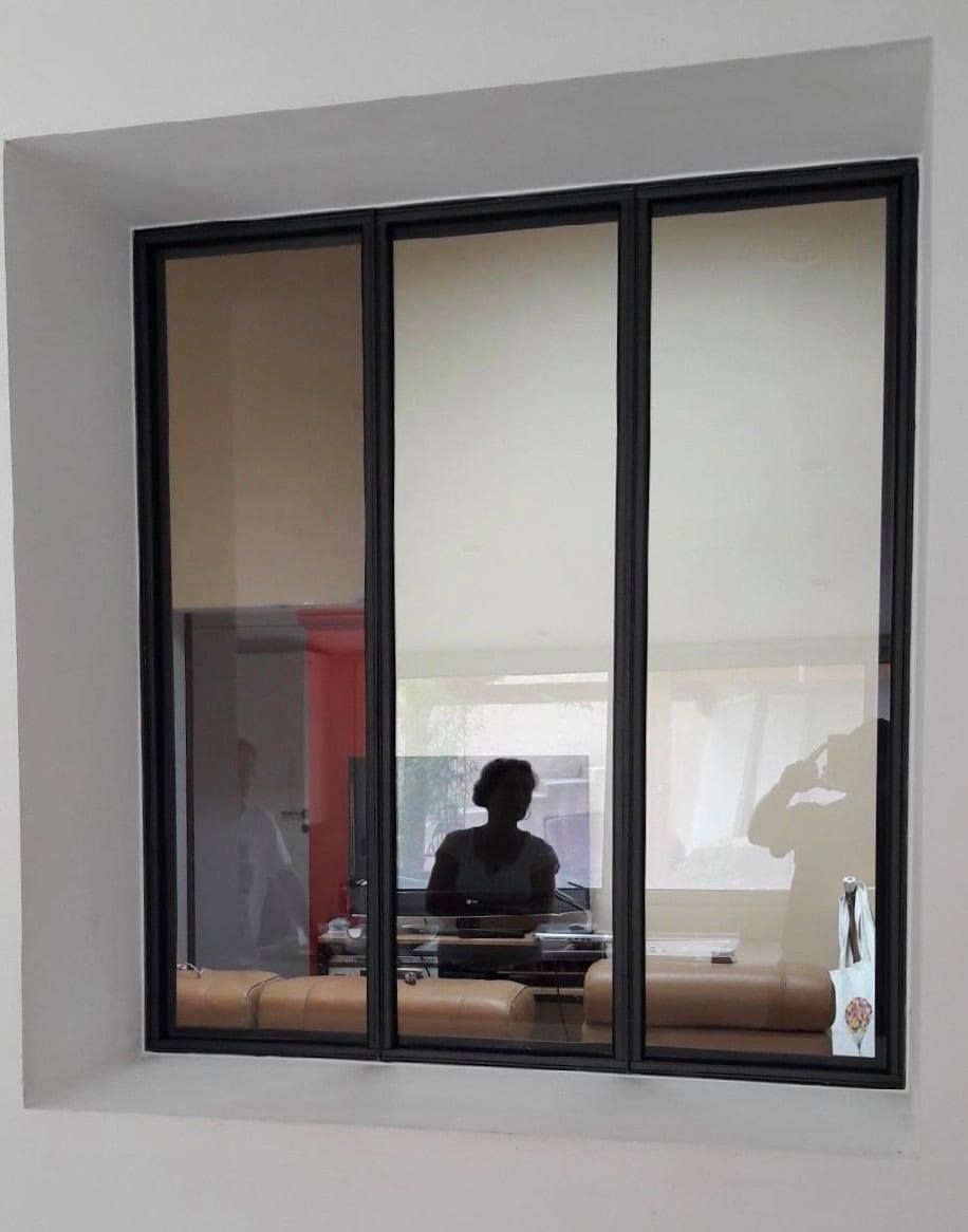 Fenêtre à cadre noir et à trois panneaux reflétant une personne à un bureau.