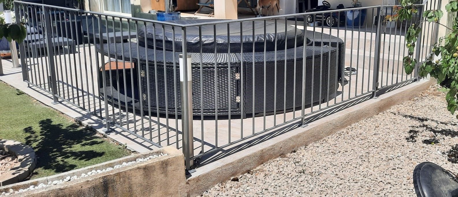 Clôture en métal noir entourant une structure circulaire, probablement un spa ou un jacuzzi extérieur, avec un sol recouvert de gravier.