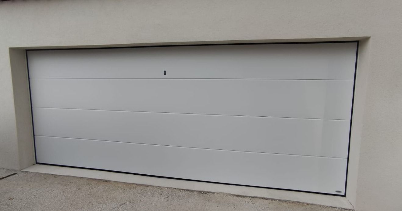 Porte de garage blanche, rectangulaire, encastrée dans un mur clair.