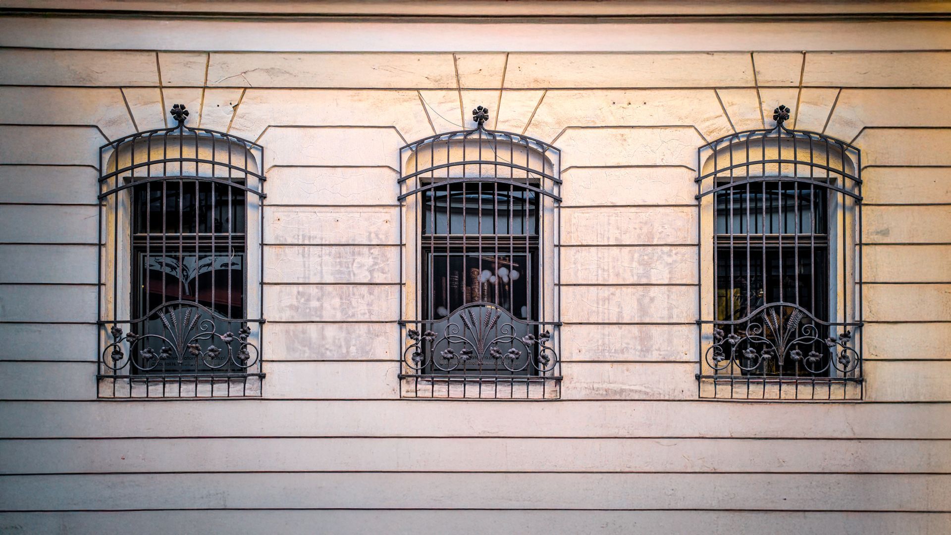 Trois fenêtres cintrées avec des barreaux de sécurité en métal ornementé sur une façade d'immeuble de couleur crème.