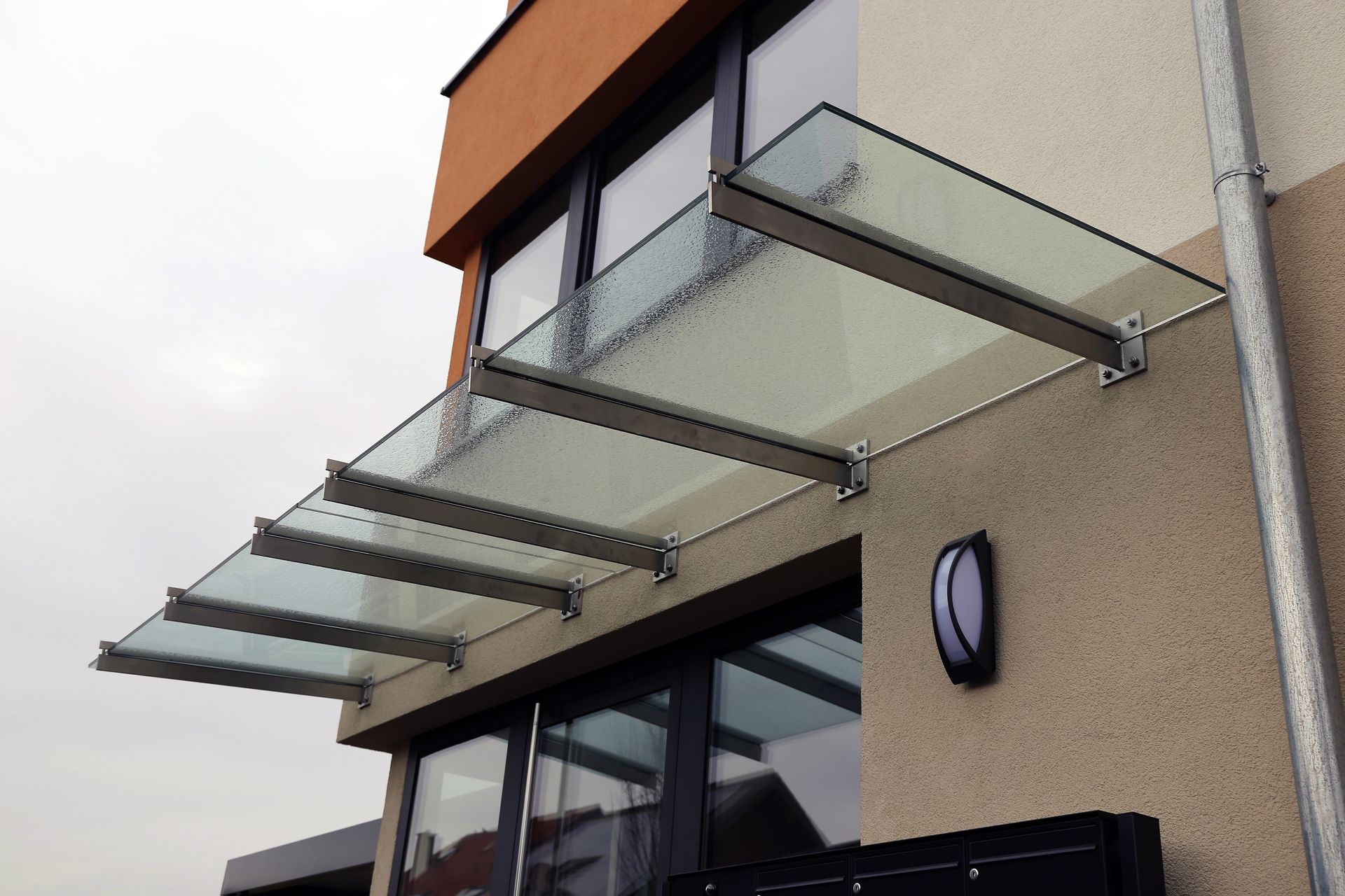 Auvent en verre au-dessus d'une fenêtre, soutenu par des supports métalliques sur un bâtiment.