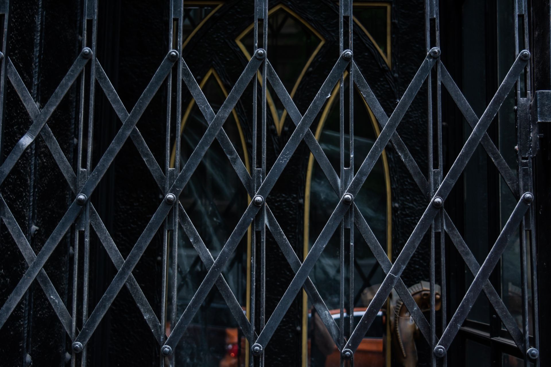Une grille de sécurité en métal noir masque partiellement une porte sombre.