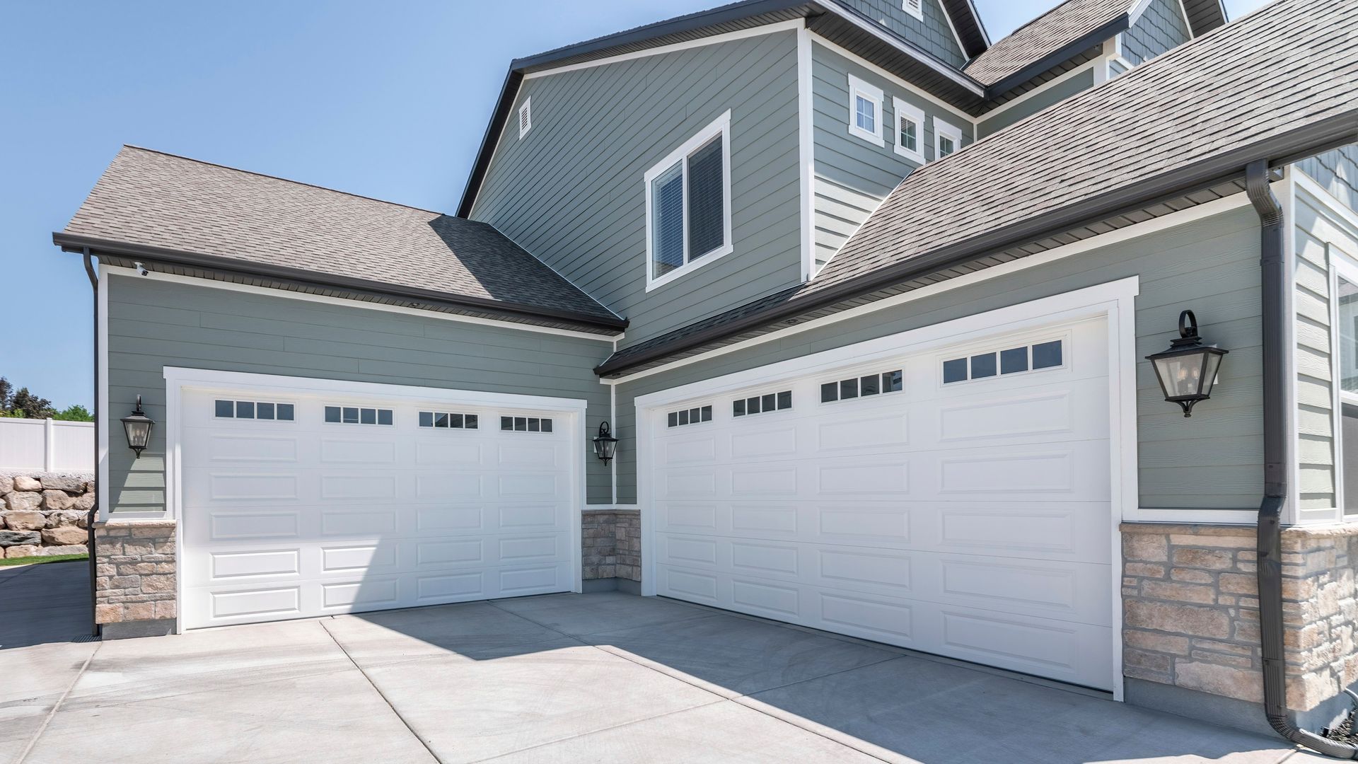 Garage double avec portes blanches sur une maison bleu-gris à deux étages.
