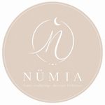 Logotipo N&Uuml;MIA en color beige con un monograma en letra cursiva blanca y el nombre de la marca sobre un fondo circular.