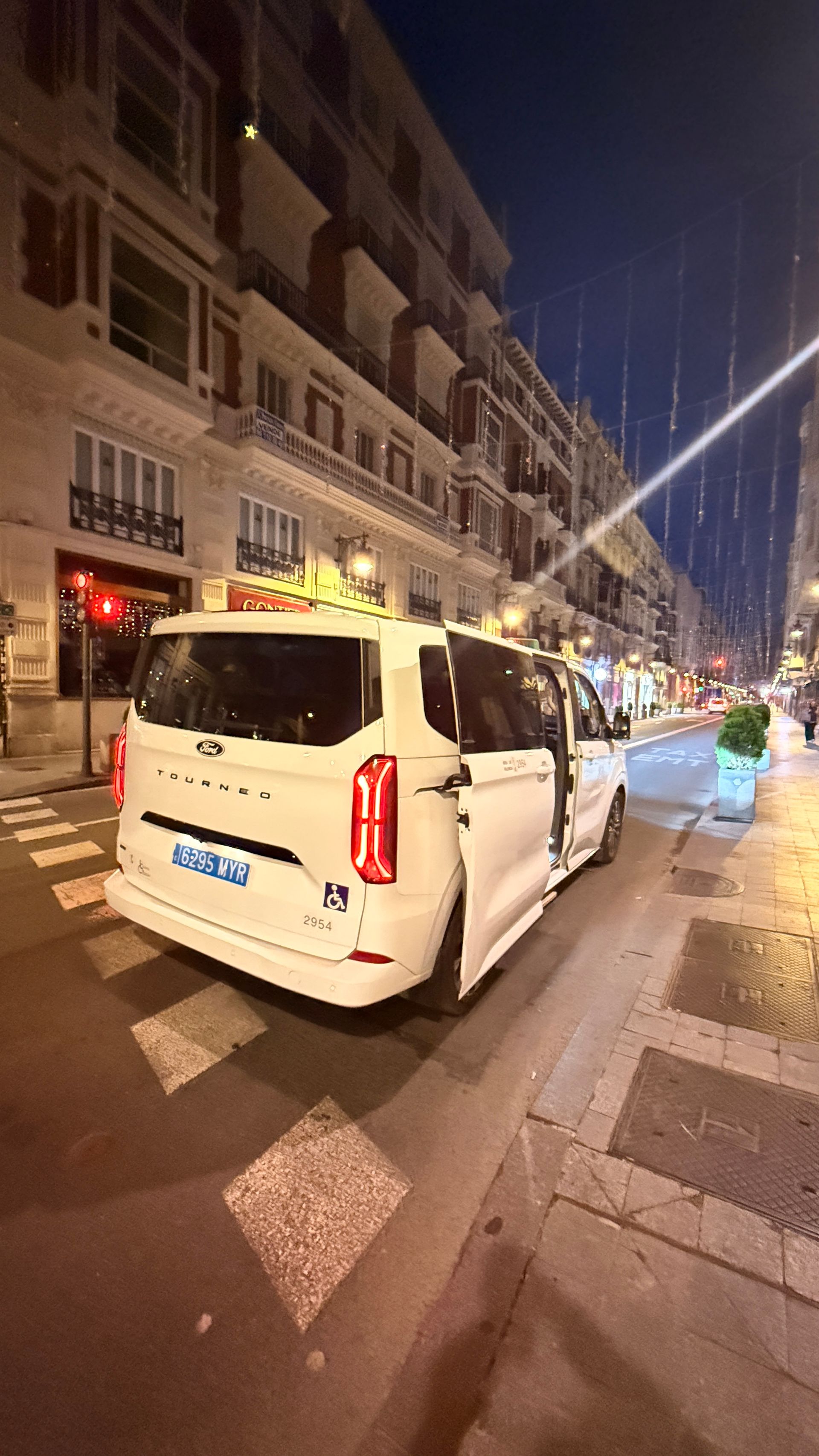 Taxi blanco estacionado en una calle de noche. Puerta abierta. Edificio con ventanas al fondo.