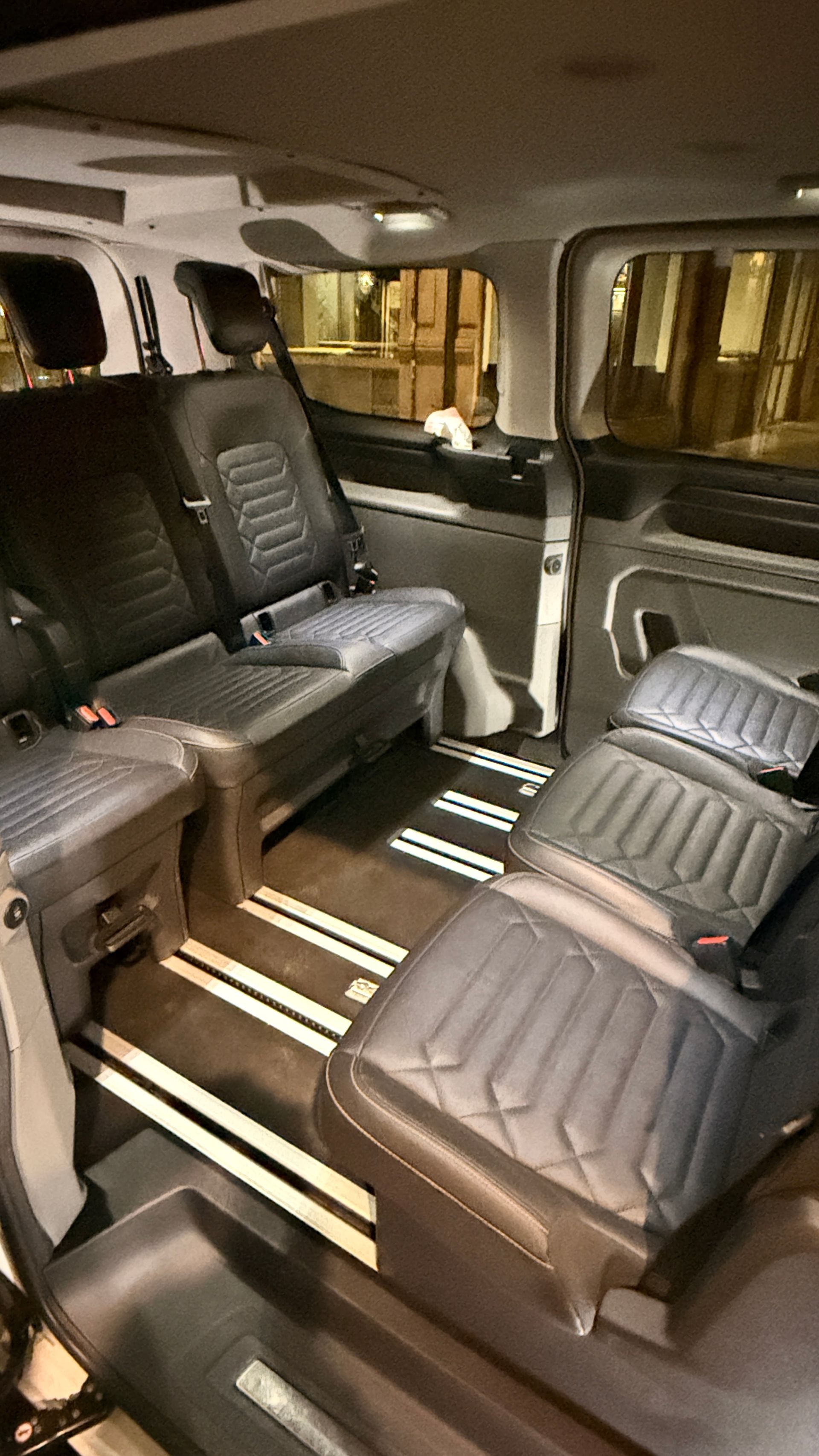 Interior de una furgoneta con asientos de cuero negro dispuestos en filas; suelo de madera.