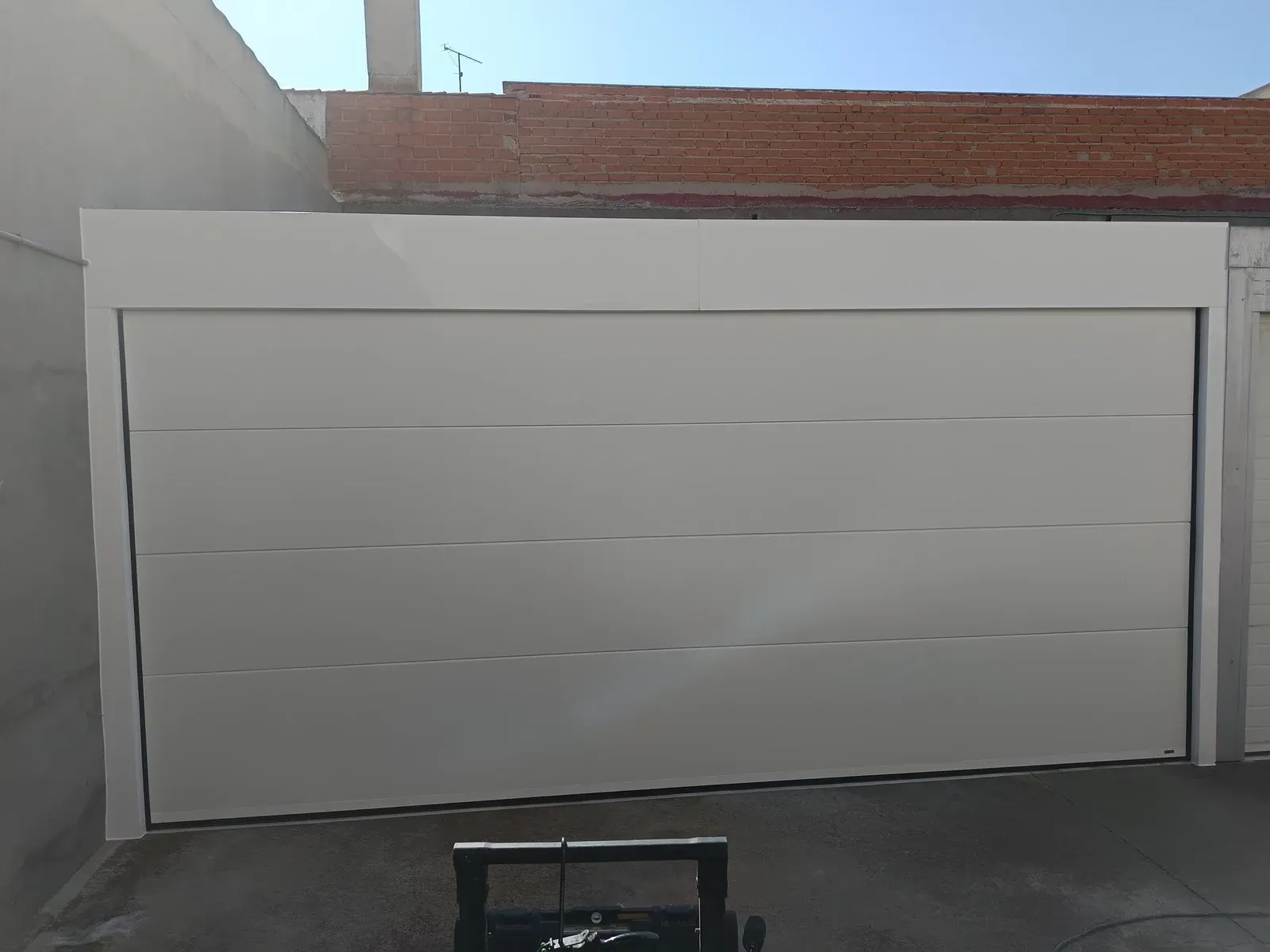 Puerta de garaje blanca, horizontal, situada entre una pared de ladrillo y una pared gris.