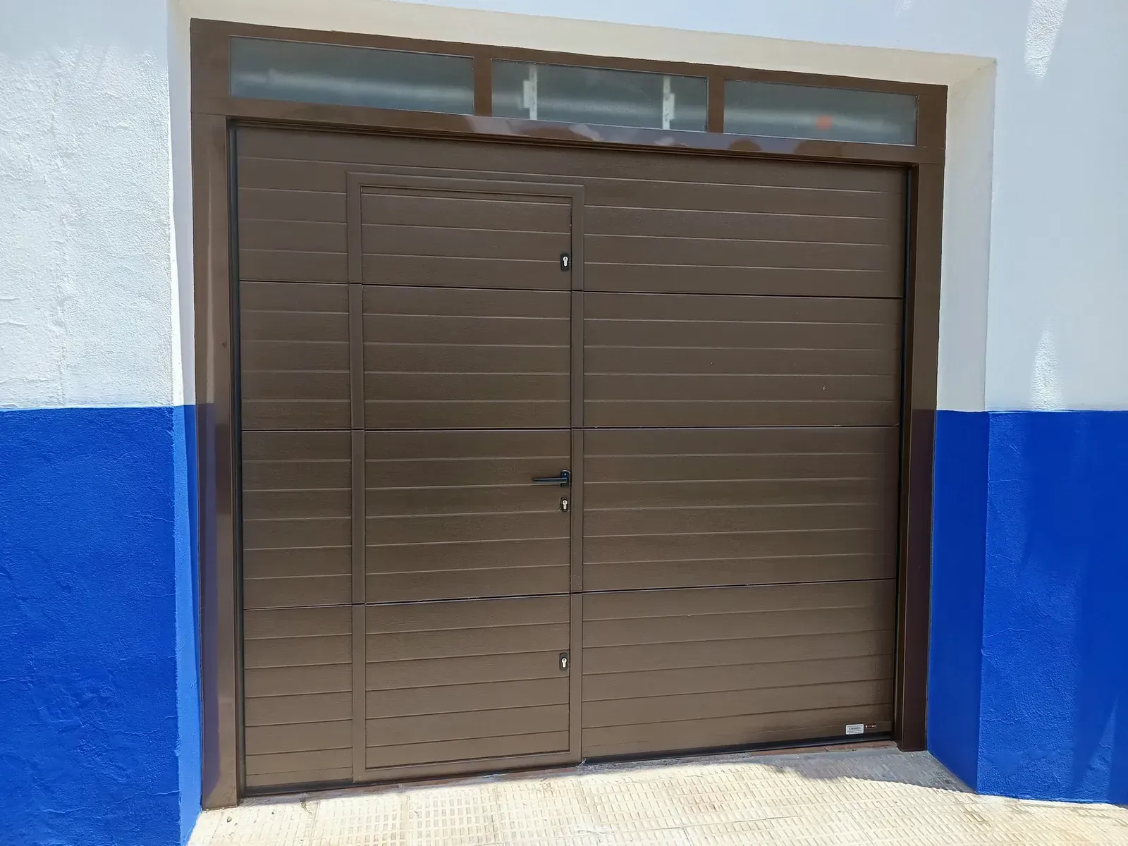 Puerta de garaje de metal marrón en una fachada de edificio blanca y azul.