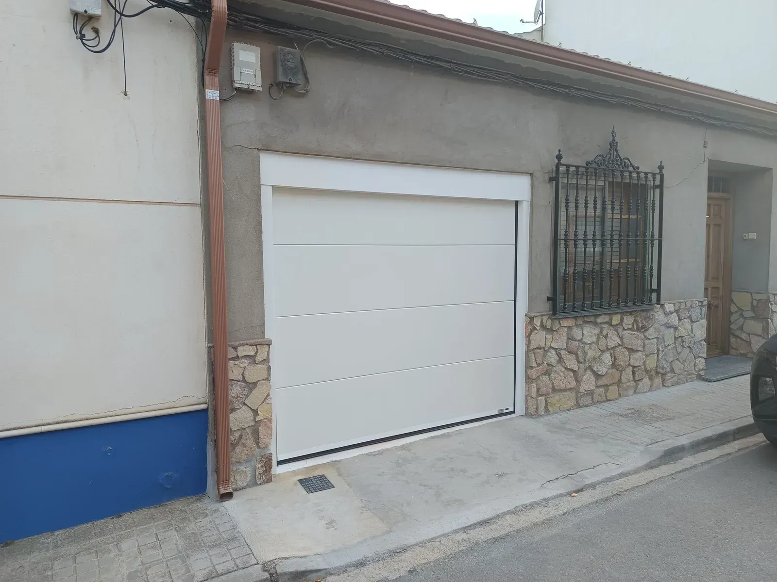 Puerta de garaje blanca en un edificio con revestimiento de piedra y rejas de hierro forjado.