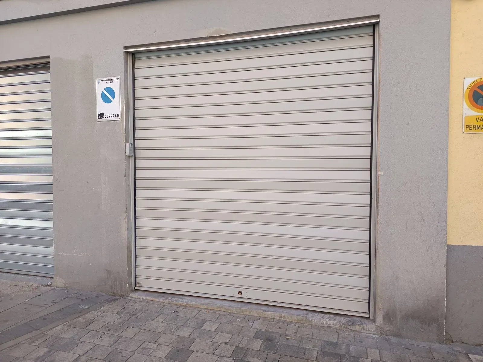 Puerta de garaje enrollable metálica gris en la fachada de un edificio. Señal de aparcamiento a la izquierda.