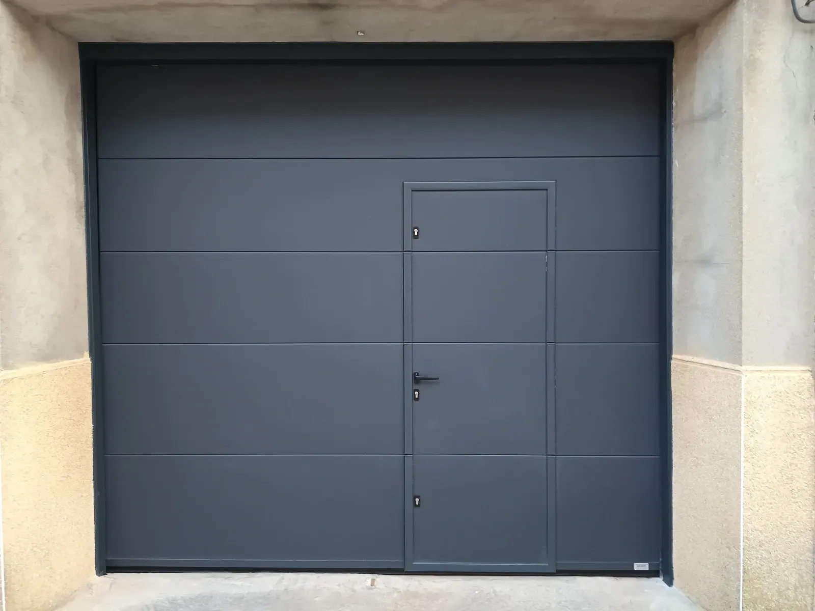 Puerta de garaje gris oscuro con una puerta integrada más pequeña.