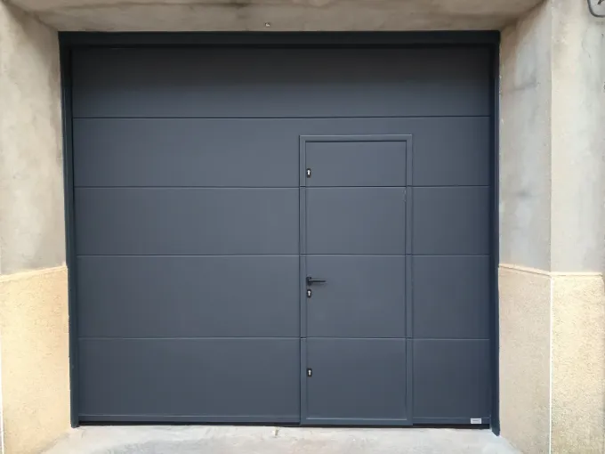 Puerta de garaje gris oscuro con una puerta integrada más pequeña.