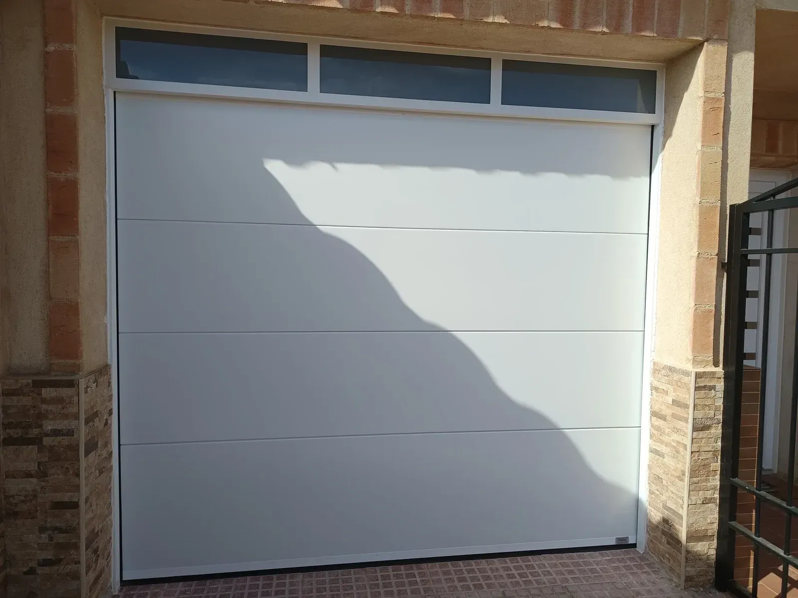 Puerta de garaje blanca con tres paneles horizontales y pequeñas ventanas en la parte superior.