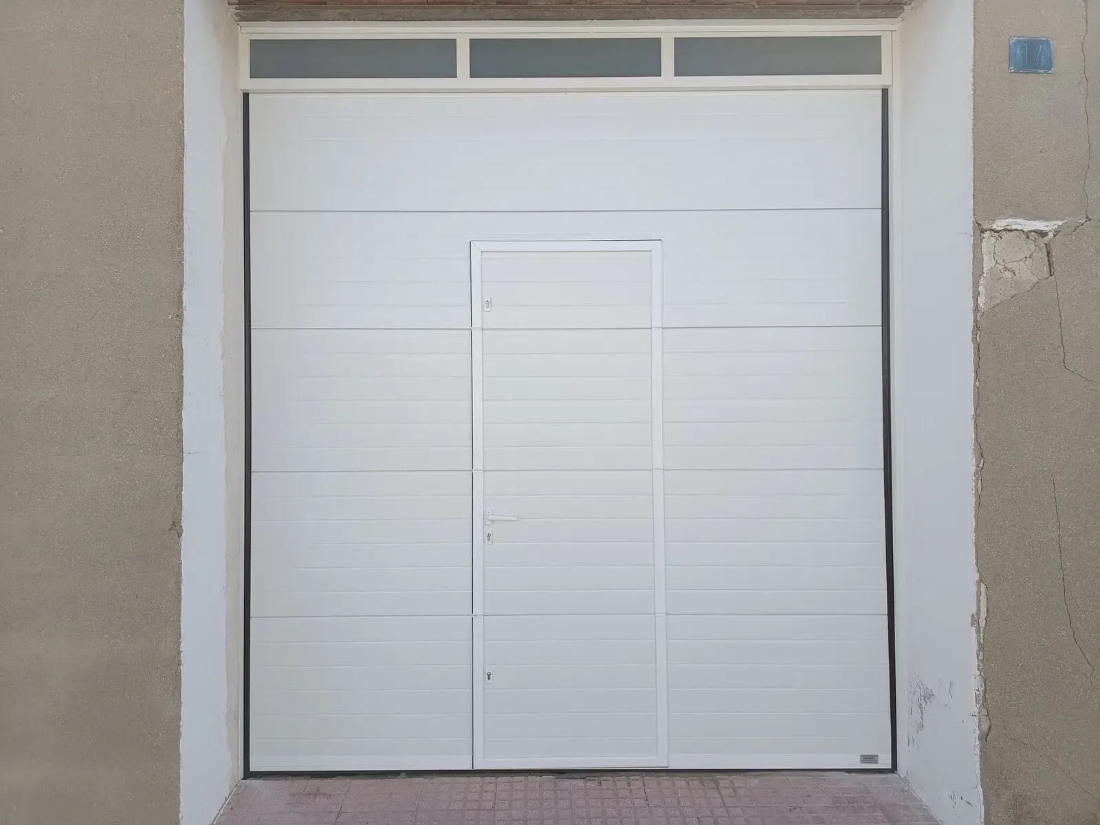 Puerta de garaje blanca con puerta peatonal integrada.