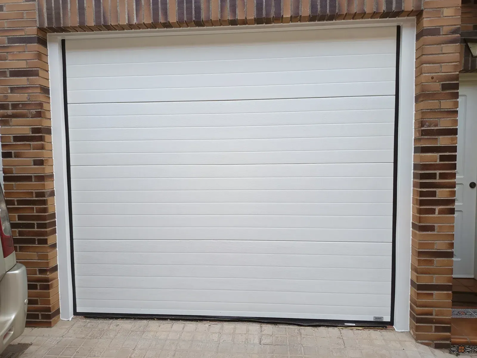 Puerta de garaje de panel horizontal blanco, enmarcada por ladrillo.