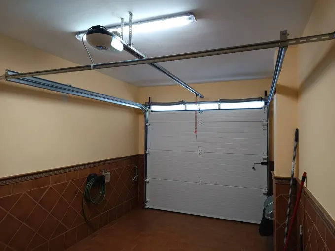 Vista interior de un garaje con la puerta basculante parcialmente abierta. Se ven las vías y el portón automático.