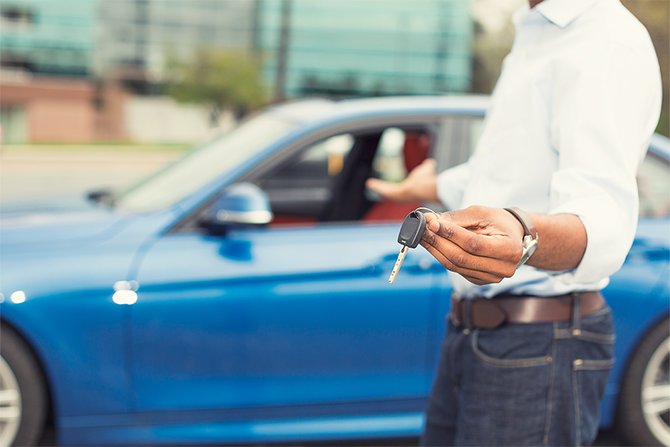 Ein Mann hält einen Autoschlüssel vor einem blauen Auto.