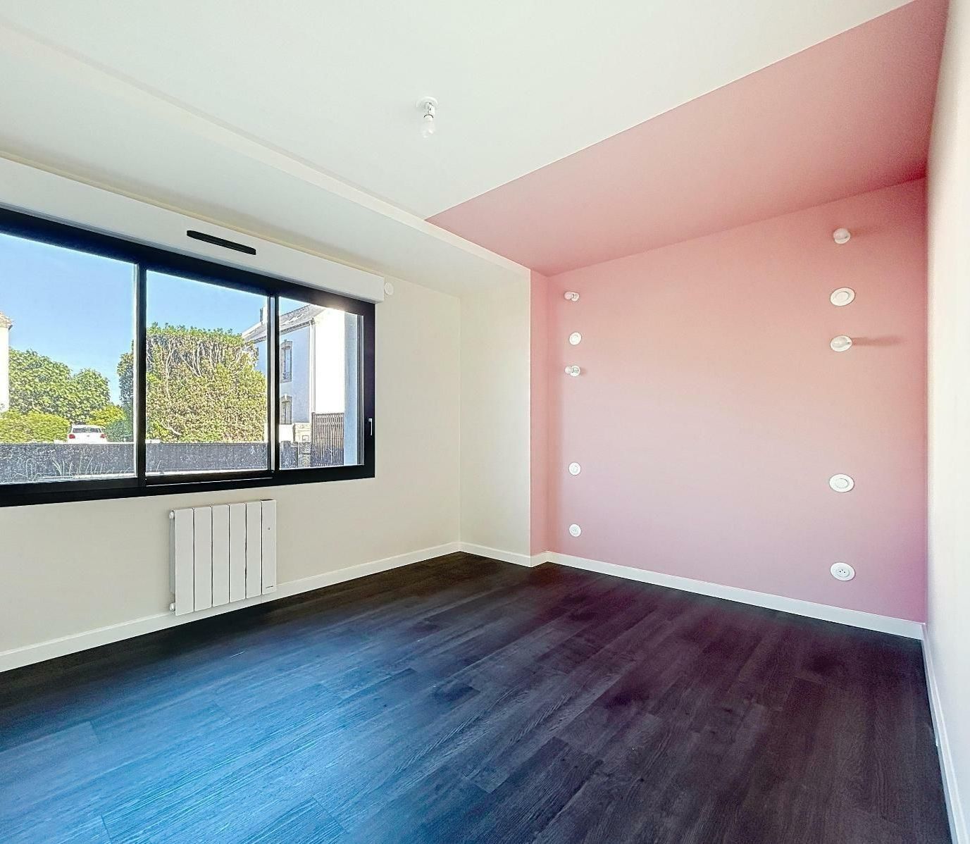 Une pièce avec le parquet au sol et un mur rose.