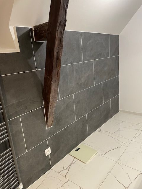 Détail d'une salle de bains avec le carrelage et une poutre en bois.