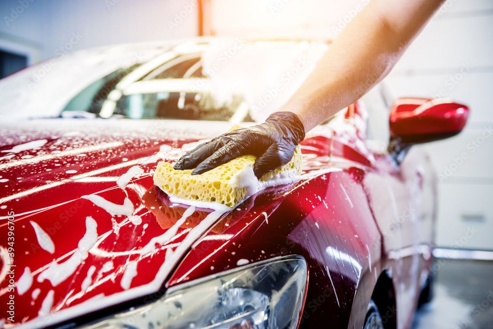 Une personne lave une voiture rouge avec une éponge.