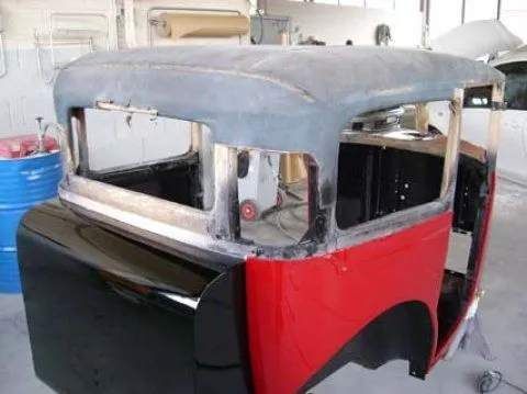 Une voiture rouge et noire est en cours de restauration dans un garage.