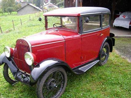 Une vieille voiture rouge est garée dans l'herbe devant un garage.