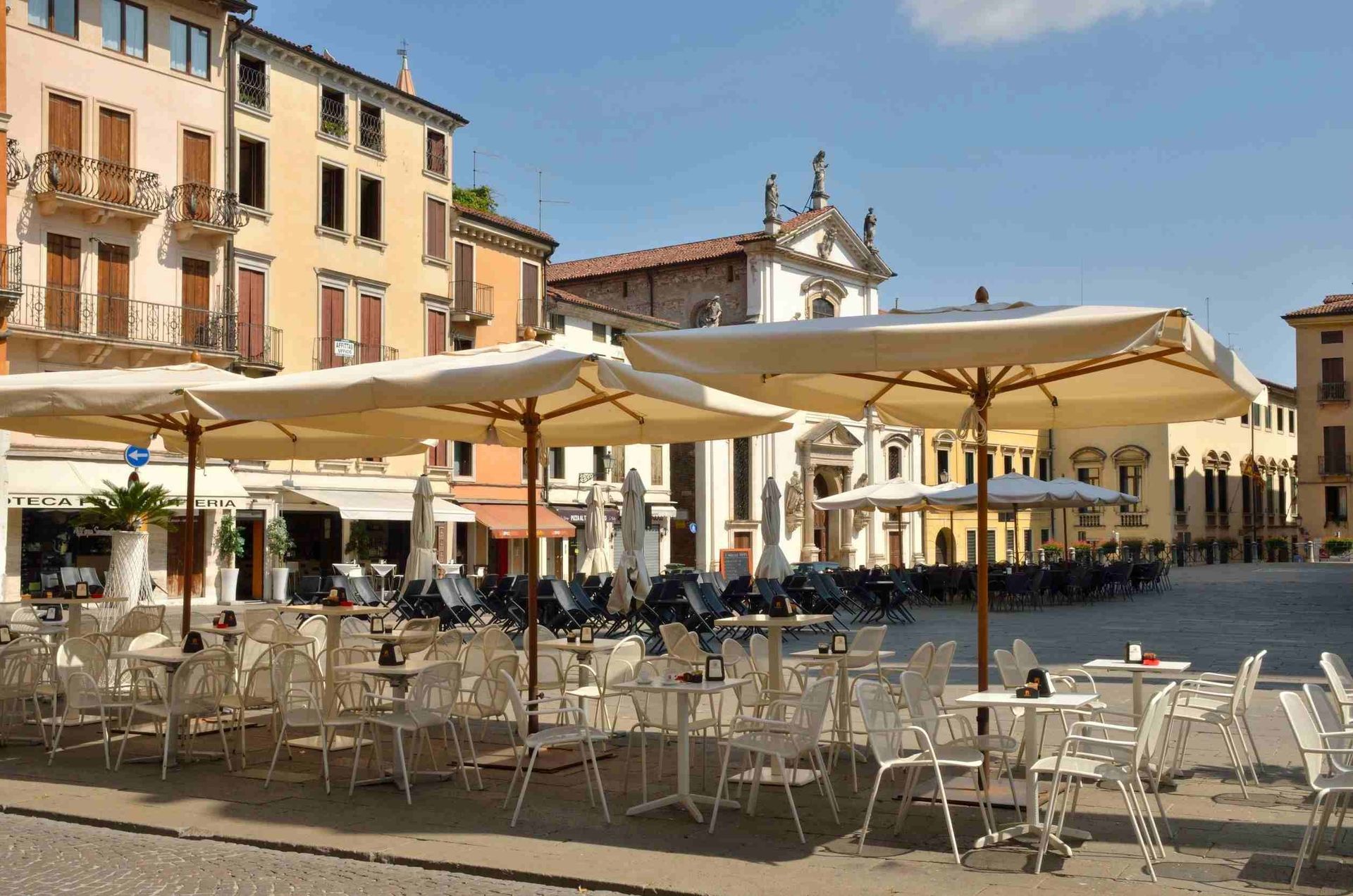 Una fila de mesas y sillas bajo sombrillas frente a un edificio.
