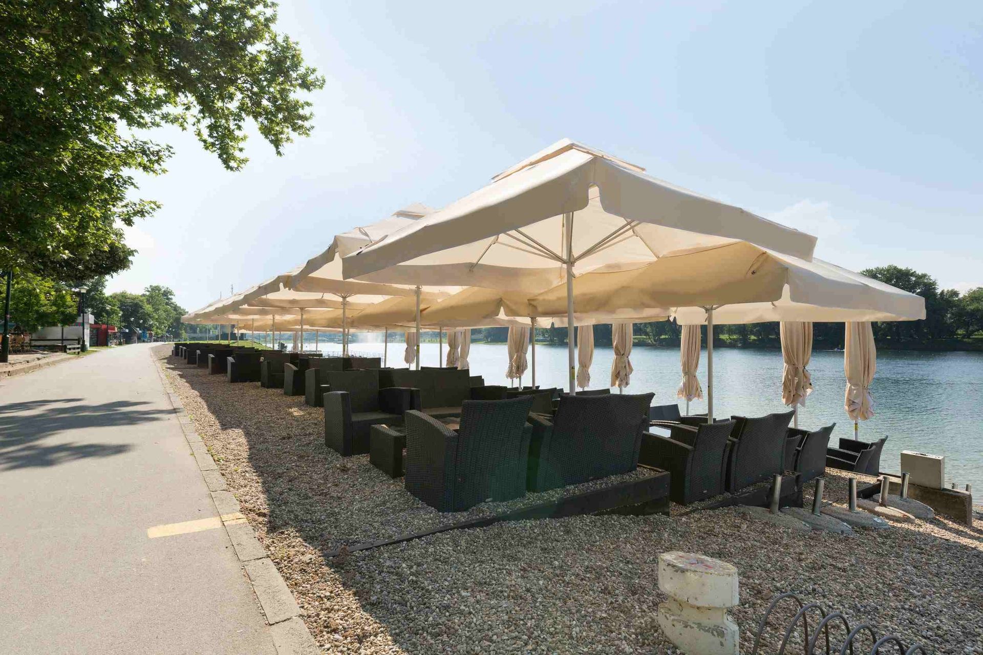 Una fila de mesas y sillas bajo sombrillas junto a un cuerpo de agua.