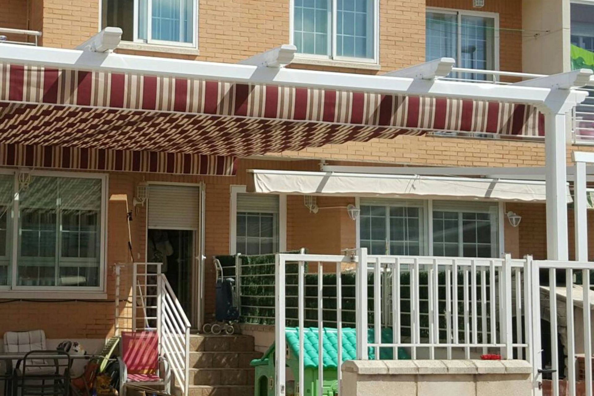 Una casa de ladrillo con una barandilla blanca y un toldo rojo y blanco