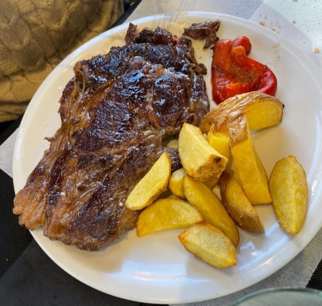 Un plato blanco cubierto con un filete y patatas gajo.