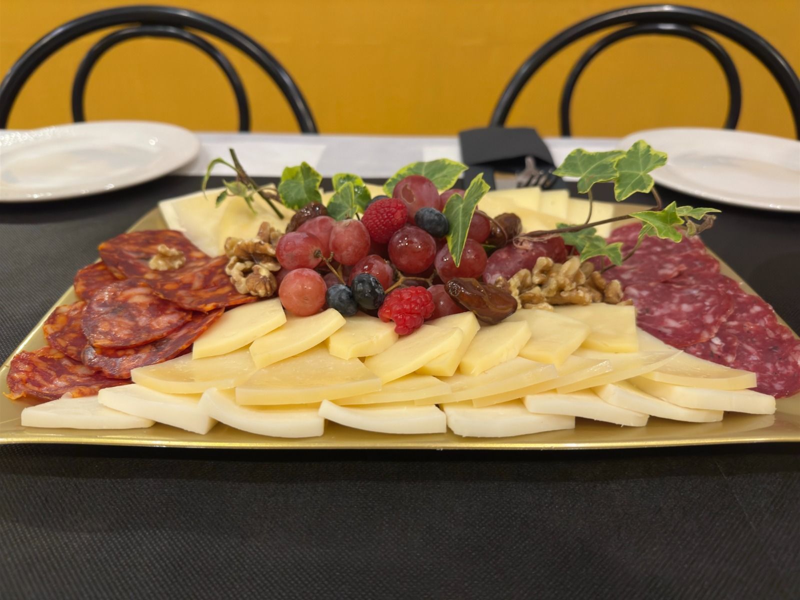 Una bandeja de carnes, quesos y bayas sobre una mesa.