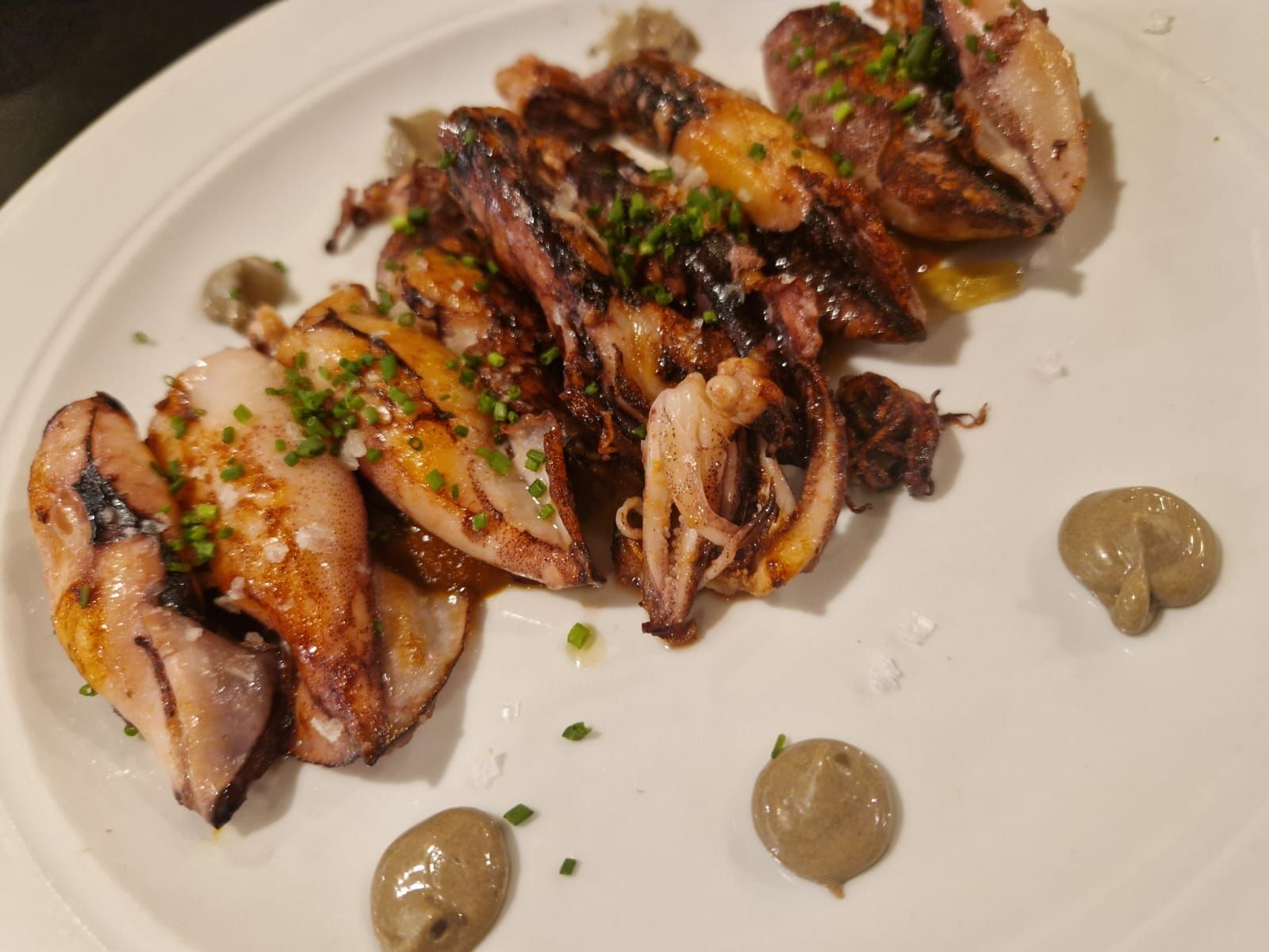 Un plato blanco cubierto con calamares y salsa sobre una mesa.