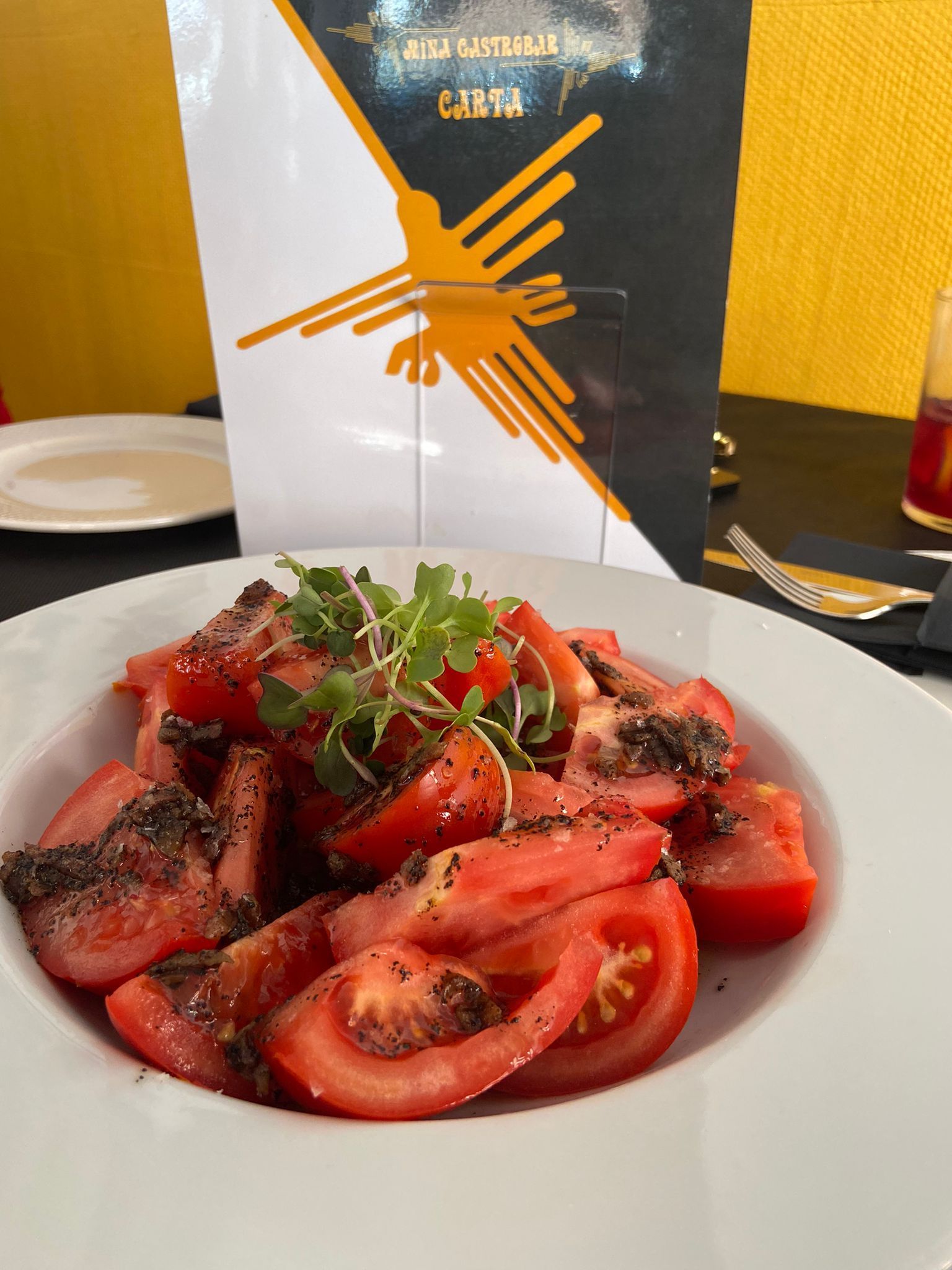 Un plato de tomates en rodajas se encuentra sobre una mesa frente a un menú.