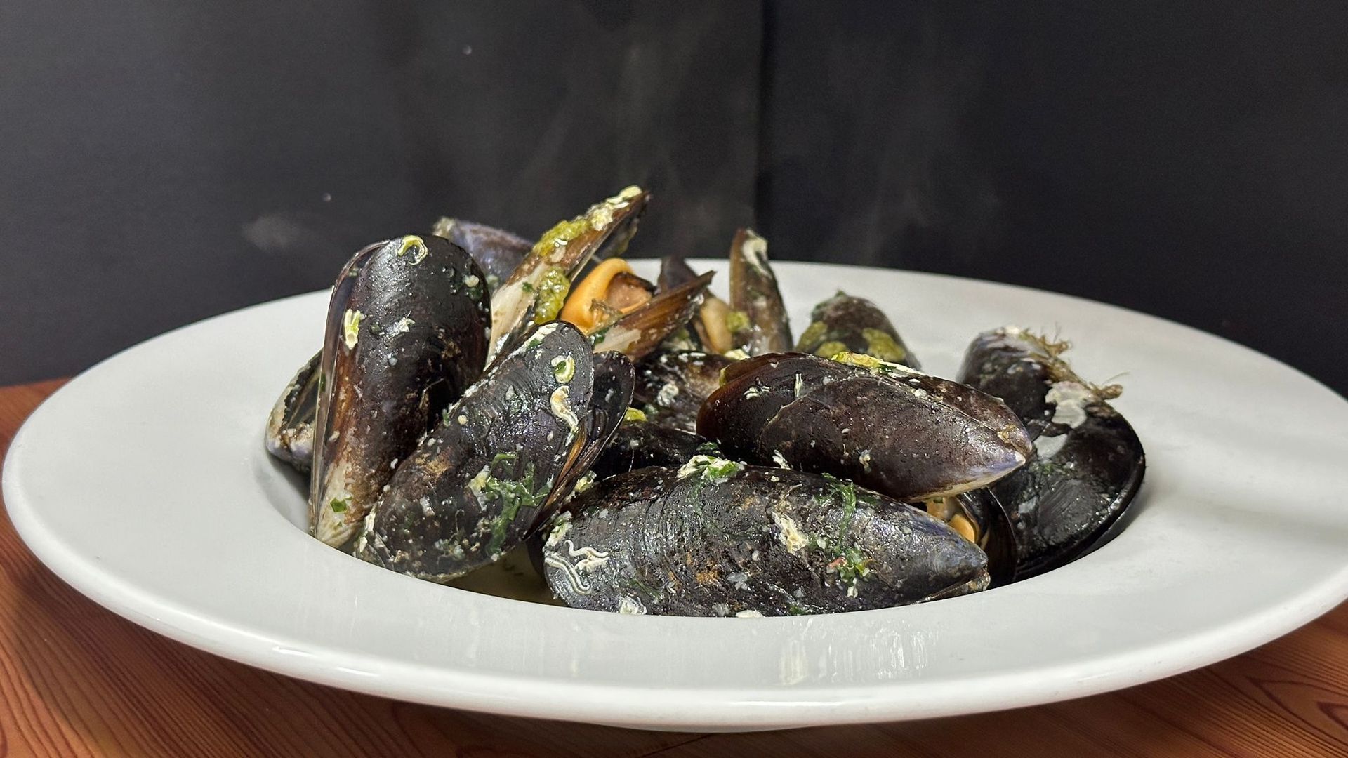 Un plato blanco cubierto de mejillones está sobre una mesa de madera.