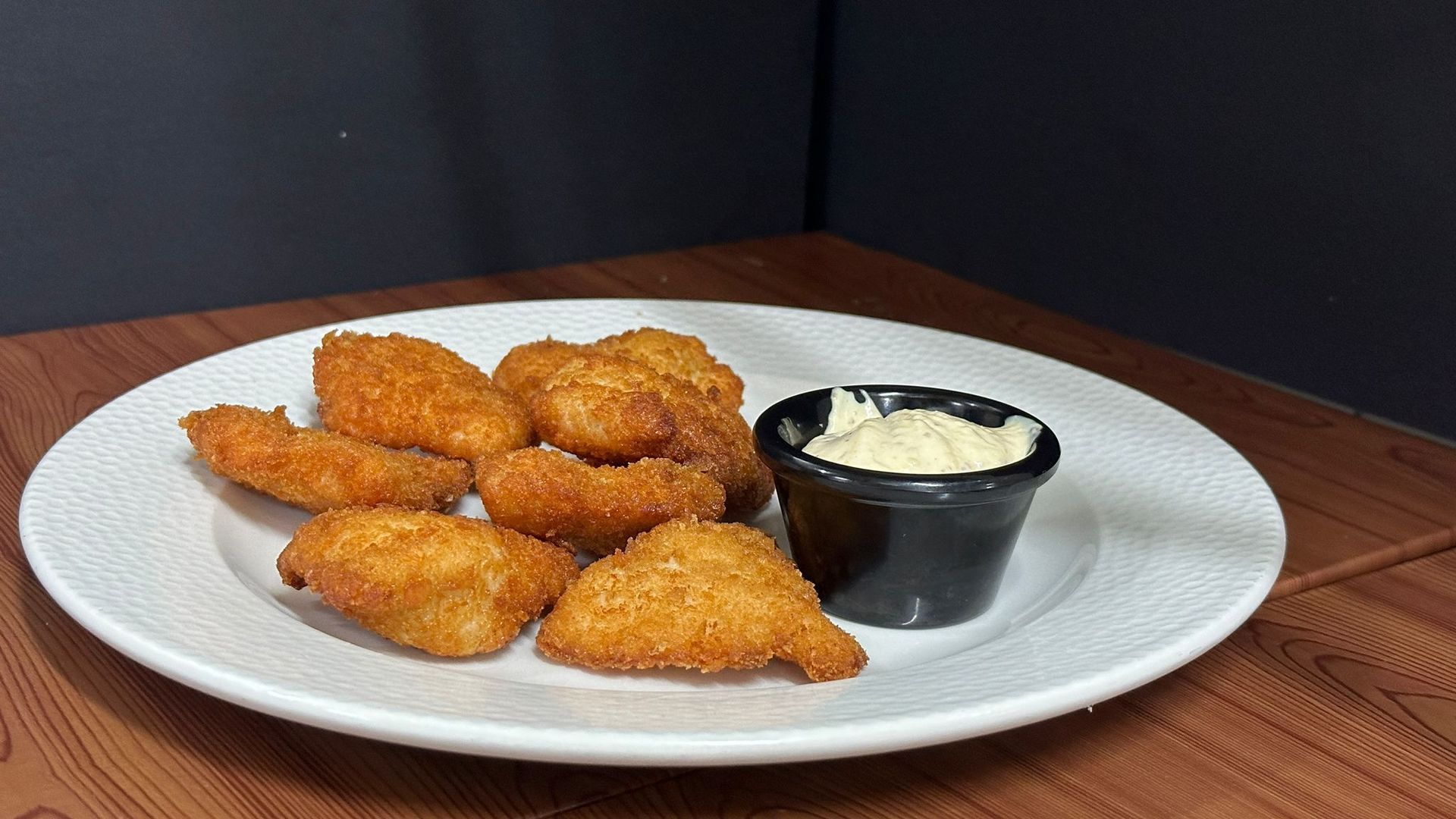 Un plato blanco cubierto con camarones fritos y un tazón pequeño de mayonesa.
