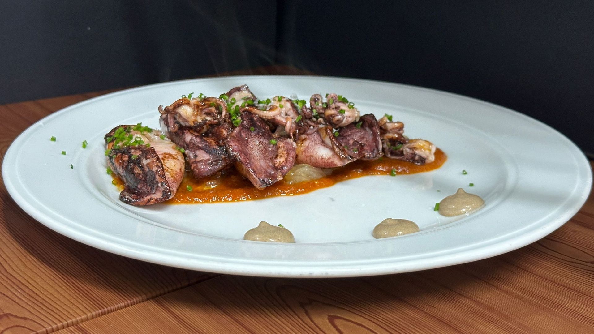 Un plato blanco cubierto con carne y salsa sobre una mesa de madera.